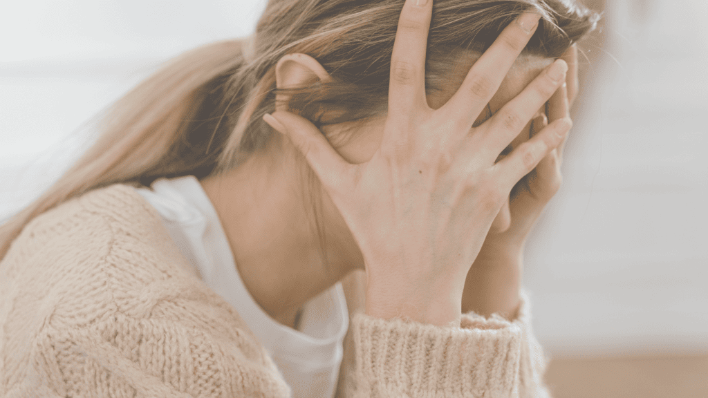 woman with long brown hair in a ponytail, beige knit pullover, hands in front of her face, holding her head, Overcoming the Victim Consciousness Stage