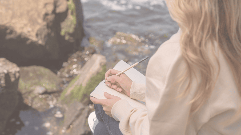 How Your Attachment Style in Relationships Lead to Divorce & 4 Ways to Create a More Secure Attachment Style | MCD woman with long blonde hair and white sweater and jeans, sitting above a water body, journaling, how to create a more secure attachment style